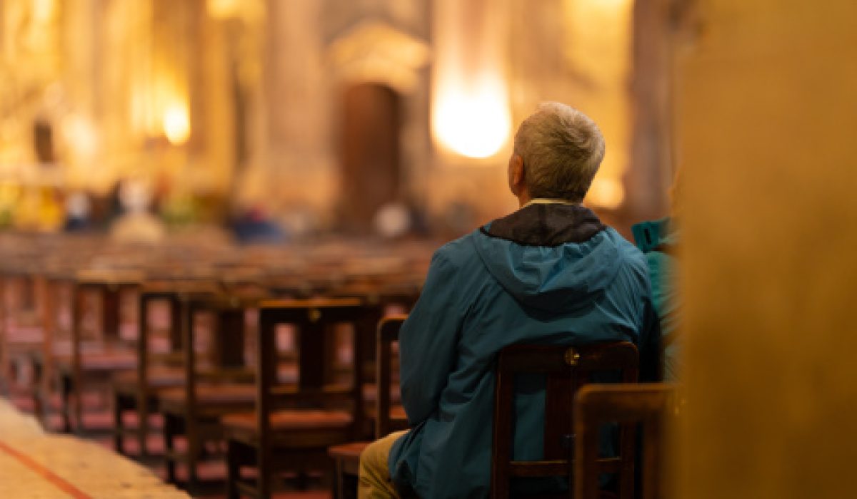 An elderly man sits at the entrance to the church and listens to a sermon